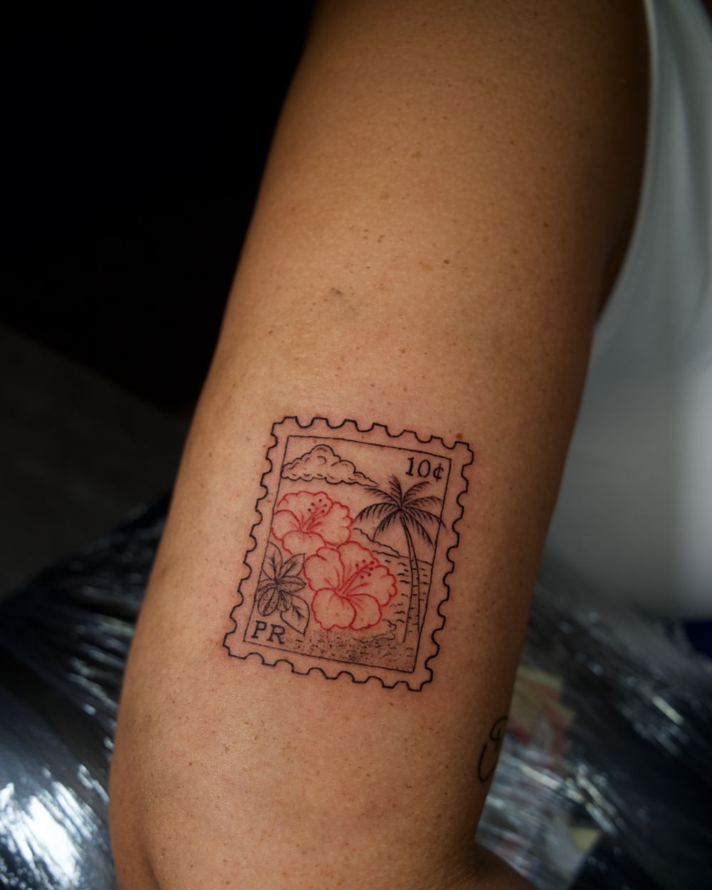 Fine-line Puerto Rico ten-cent stamp tattoo with hibiscus and palm on the arm, by Rodney Alacan