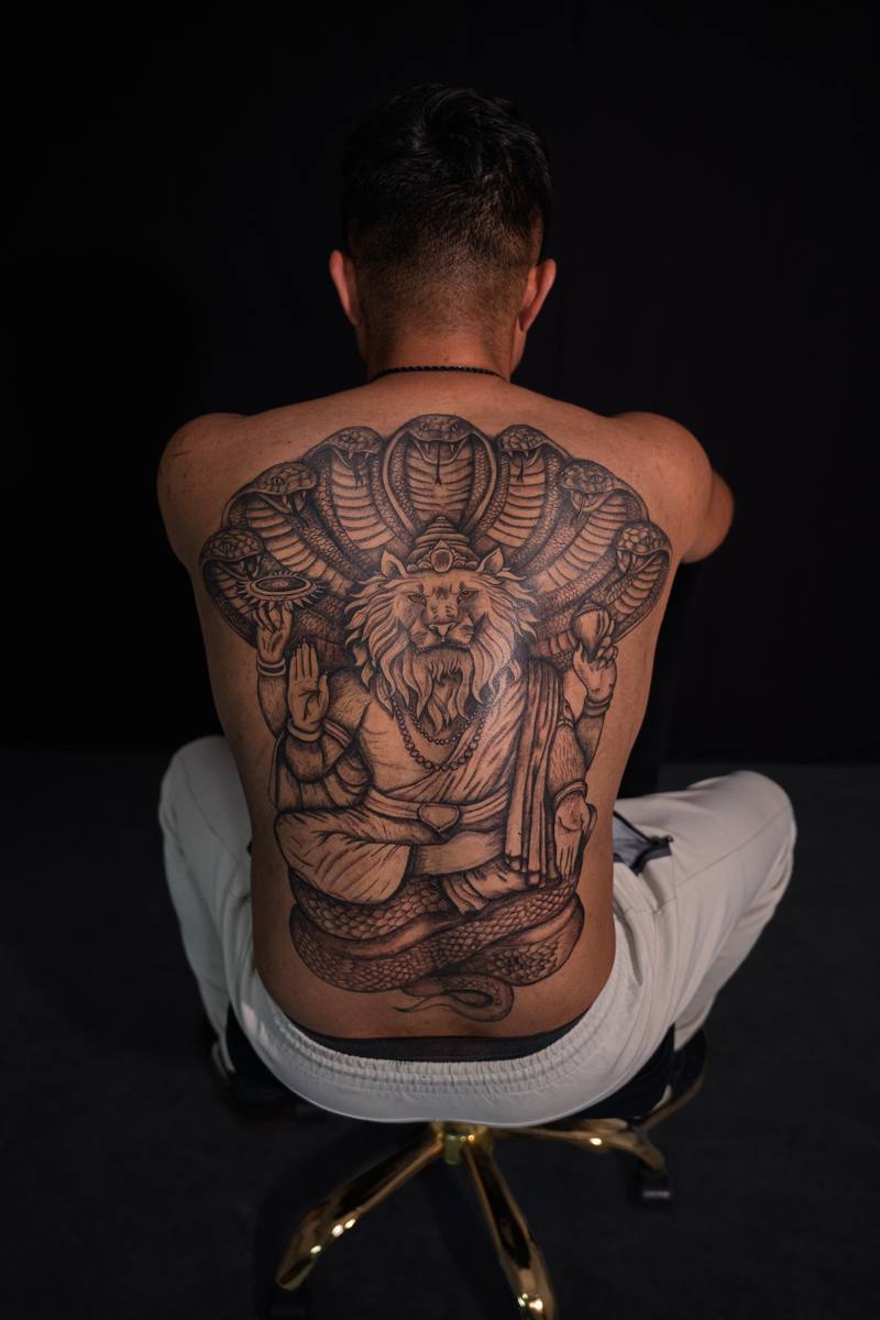 Full-back black and grey tattoo of a lion deity crowned by seven cobras, by Rodney Alacan at Golden Ink