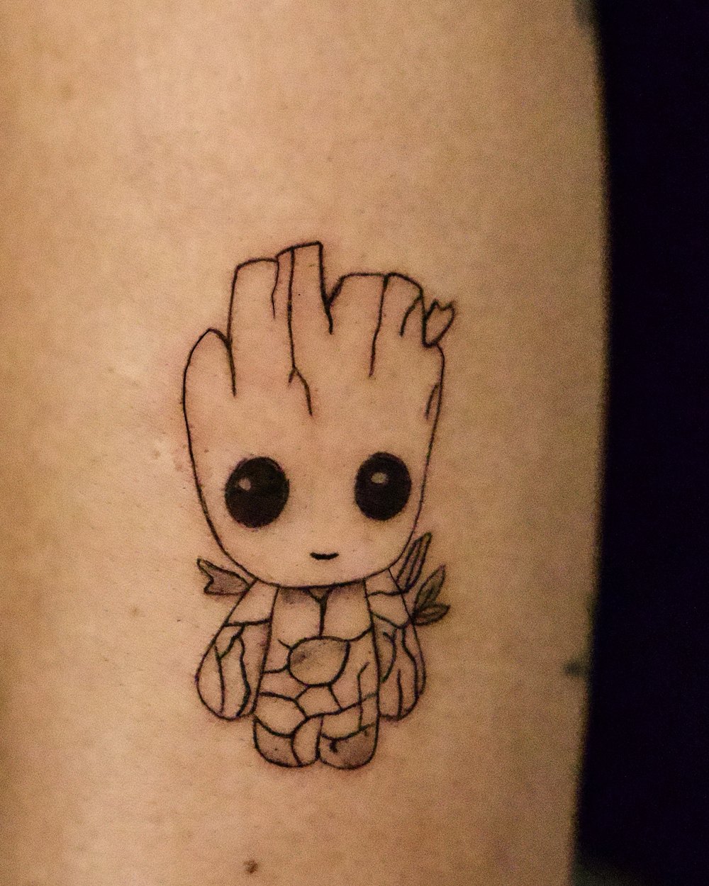 Small fine-line Groot tattoo on the upper arm, by Israel Crespo