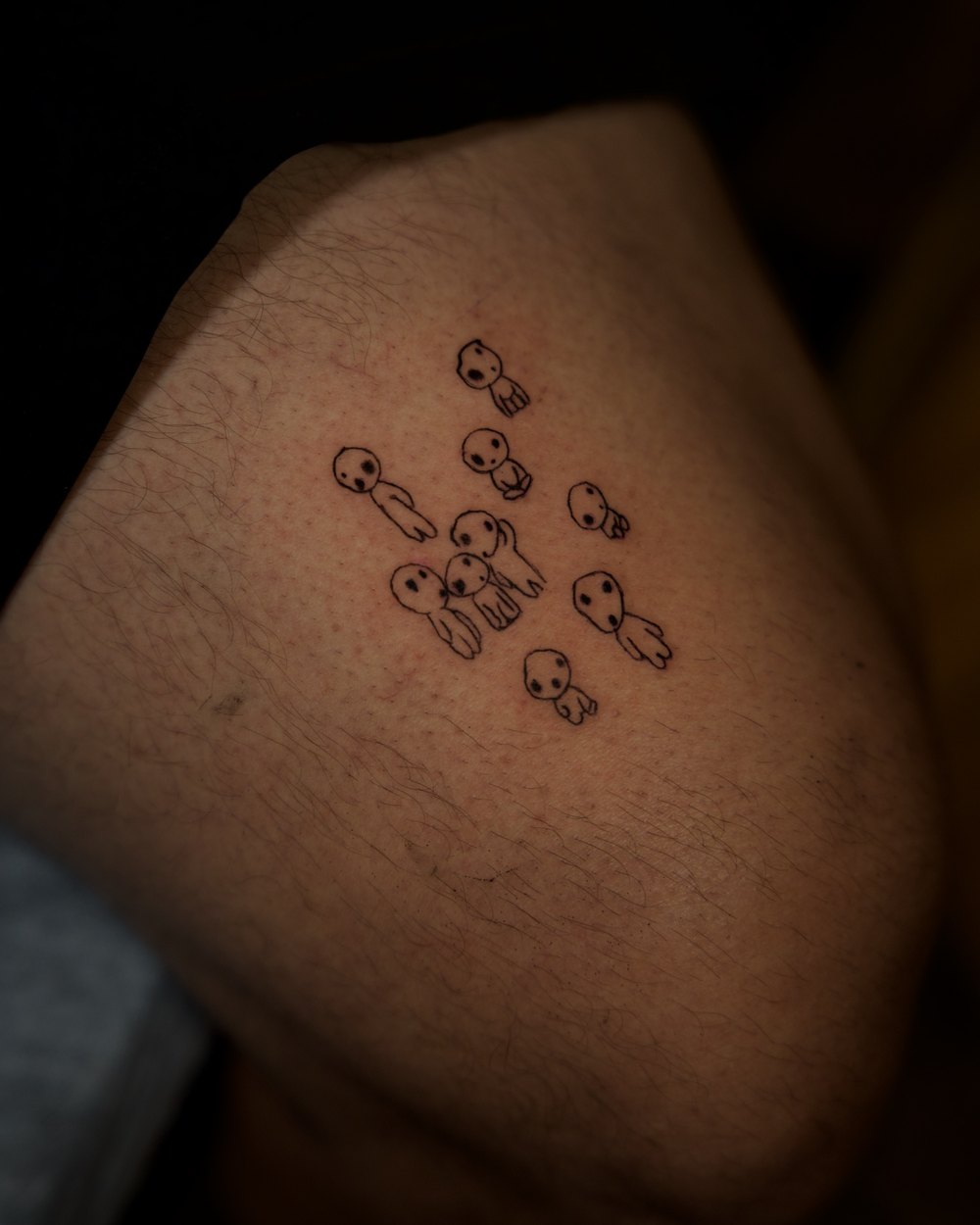 Group of small forest-spirit characters tattooed above the knee, by Israel Crespo